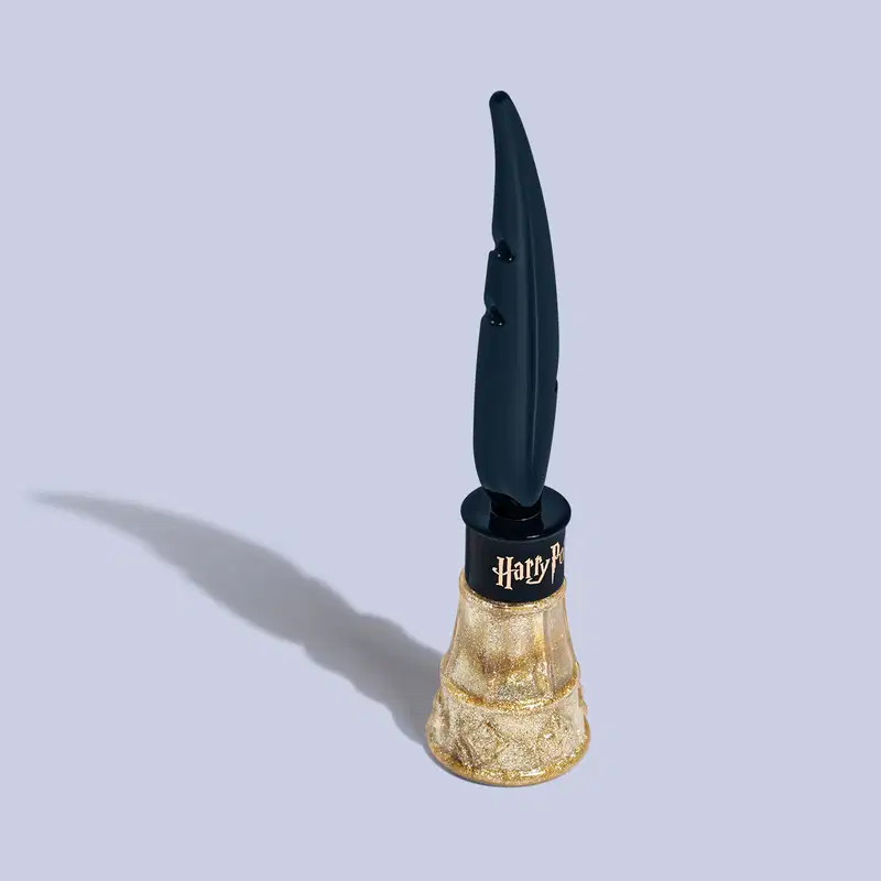 Frasco com formato alongado e curvilíneo. A parte inferior é dourada com brilhos. O frasco tem um aplicador em forma de pena alongada na parte superior, na cor azul. Na base da tampa, a logo "Harry Potter" em letras estilizadas na cor dourado brilhante.