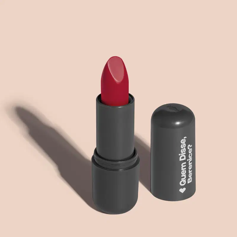 O produto apresentado na imagem é um batom da marca Quem Disse, Berenice?. O batom possui uma embalagem preta com o logotipo da marca impresso. A cor do batom é um rosa brilhante. O formato do batom é cilíndrico, com uma ponta arredondada.