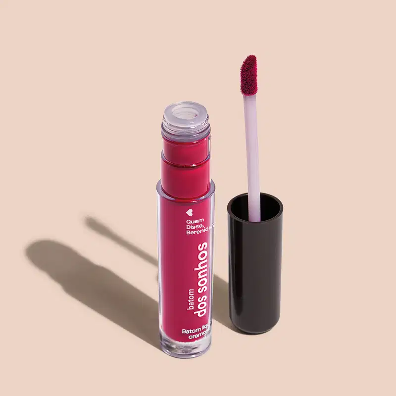 Batom líquido Rosa em frasco transparente de plástico, com aplicador de espuma na cor rosa. O frasco possui uma tampa protetora preta para guardar o aplicador. O rótulo no frasco exibe o nome da marca e do produto em letras brancas sobre fundo rosa.