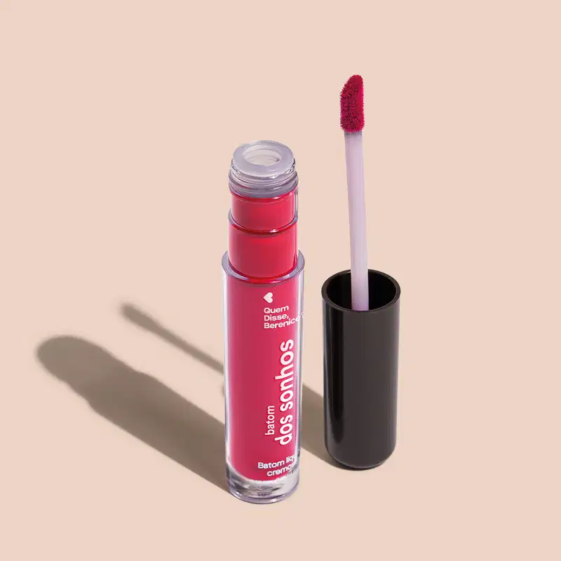 Batom líquido Rosa em frasco transparente de plástico, com aplicador de espuma na cor rosa. O frasco possui uma tampa protetora preta para guardar o aplicador. O rótulo no frasco exibe o nome da marca e do produto em letras brancas sobre fundo rosa.