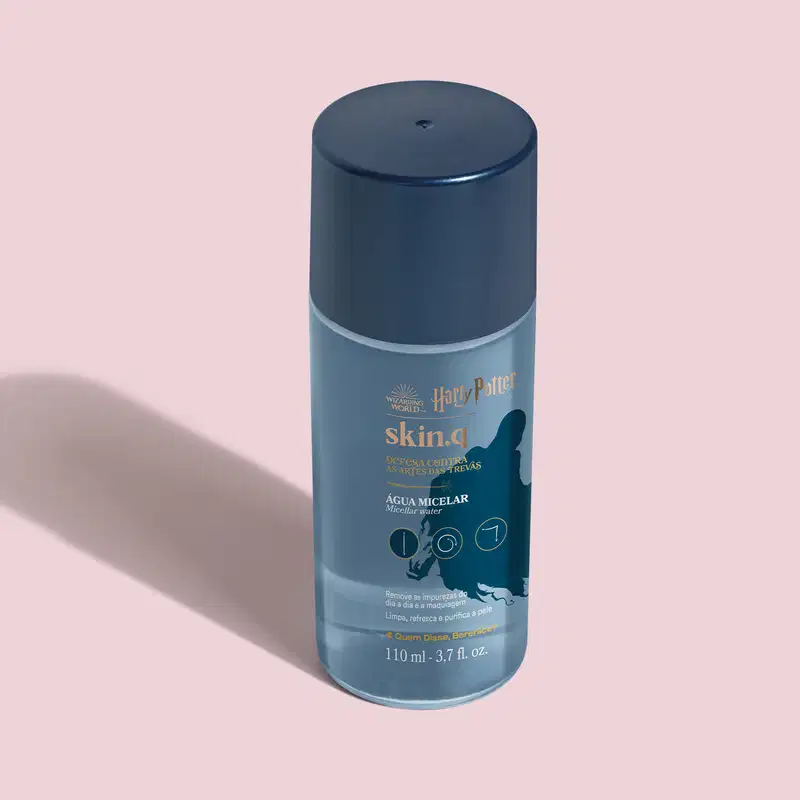 O frasco contém um produto líquido chamado "Skin.q Água Micelar" da linha Harry Potter. A embalagem apresenta detalhes em tons de azul claro e branco, incluindo o logotipo da marca Harry Potter, o nome do produto "Defesa Contra a Arte das Trevas."
