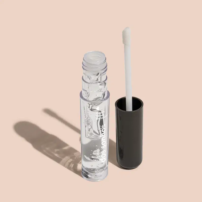A imagem mostra o frasco do gloss labial e ao lado há um aplicador de espuma na cor branca com a ponta branca e base preta.