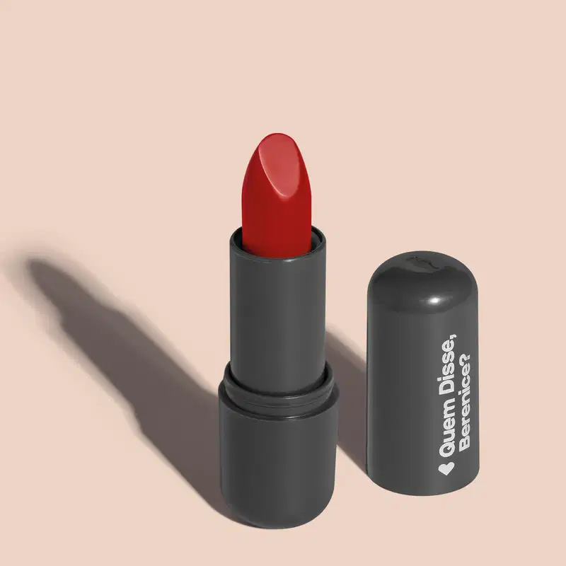 O produto apresentado na imagem é um batom da marca Quem Disse, Berenice?. O batom possui uma embalagem preta fosca e o produto em si é de cor vermelha intensa. O rótulo na embalagem exibe o nome da marca "Quem Disse, Berenice?" em letras brancas.
