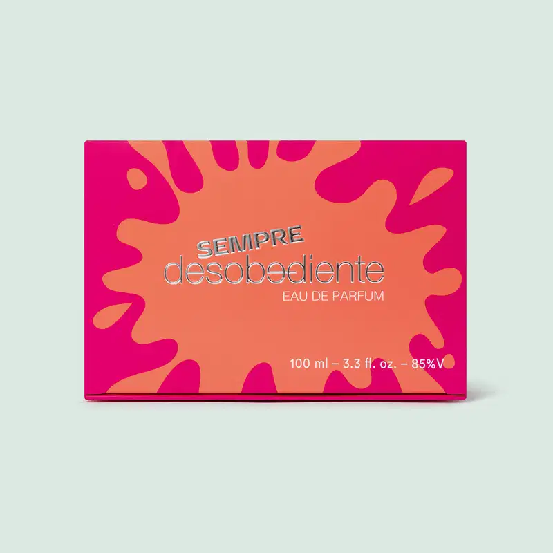 Caixa retangular. A embalagem tem fundo laranja e padrão abstrato em tons de rosa vibrante. O nome do produto "Sempre desobediente Eau de Parfum" está escrito em letras prateadas no centro. O design é chamativo, com rosa contrastando com o laranja.