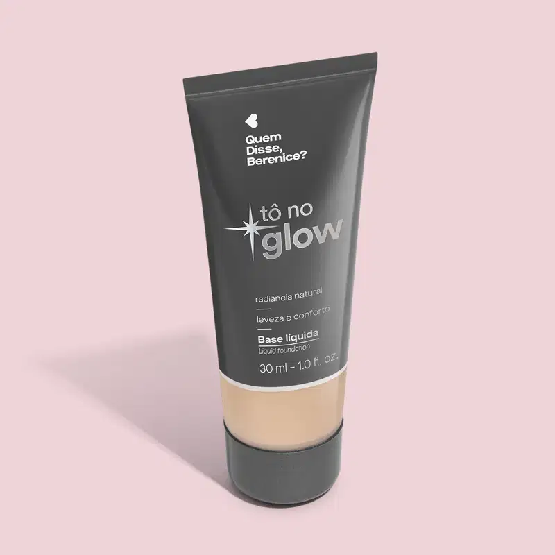 Base líquida em bisnaga preta com base transparente onde é possível ver o tom do produto. Fundo rosa.