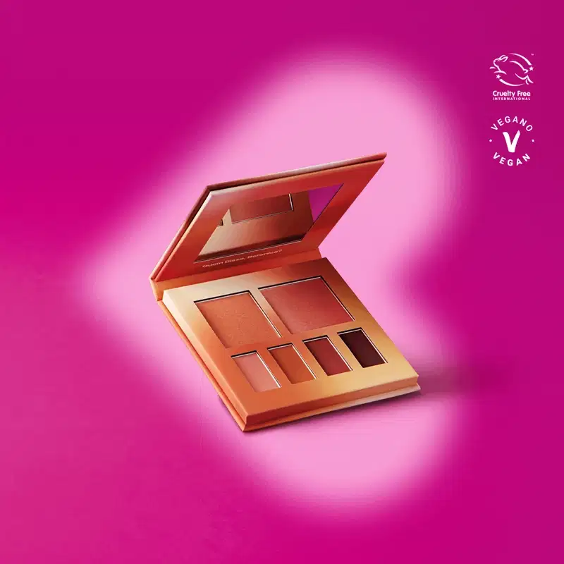Paleta ee maquiagem multifuncional Nudelele Quem Disse, Berenice? em estojo na cor rosa com espelho na tampa contendo seis cores diferentes de sombras e blushes em tons de nude em fundo roxo com sombras em volta do produto.