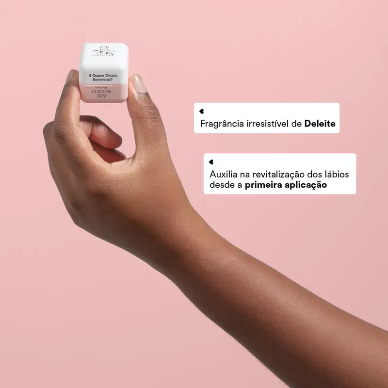 O produto é um hidratante labial da marca Quem Disse, Berenice?. Apresenta uma embalagem pequena e quadrada de cor branca. Há textos sobre ser uma "Fragrância irresistível de Deleite" .A imagem mostra uma mão segurando o produto sobre um fundo rosa claro.