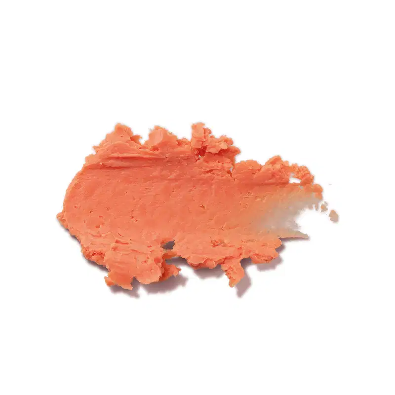 Textura cremosa e densa de tom laranja claro, com superfície irregular e ondulada, espalhada sobre fundo branco, ocupando boa parte da imagem.