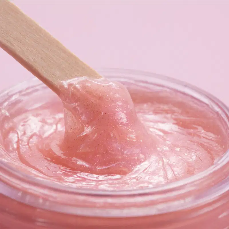 Recipiente rosa contendo um creme gelatinoso de tom rosado, apoiado sobre uma superfície lisa e brilhante.