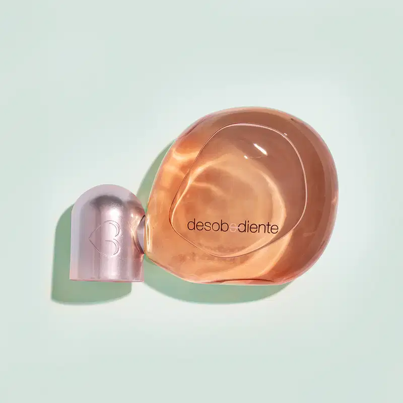 Frasco com líquido rosa e detalhes rose gold contendo 100ml de Eau de Parfum Desobediente Quem Disse, Berenice? em fundo azul claro.