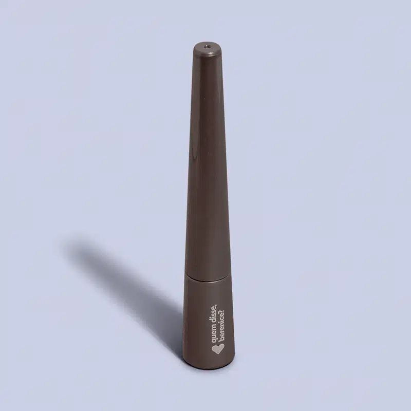 Produto de beleza em embalagem metálica cinza escuro, um frasco e um lápis. O frasco possui um rótulo com um coração, uma ponta preta e uma extremidade oca.