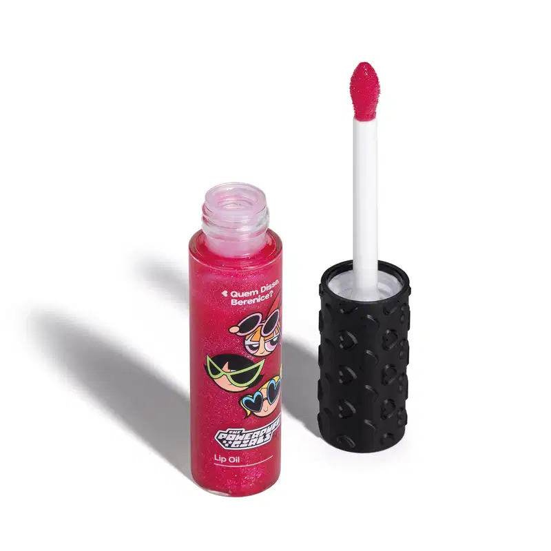 Frasco de lip oil na cor rosa da marca Meninas Superpoderosas Quem Disse, Berenice? em embalagem transparente mostrando a tonalidade do produto, tampa preta com haste e esponjinha vermelha, mostrando ilustração de personagens.