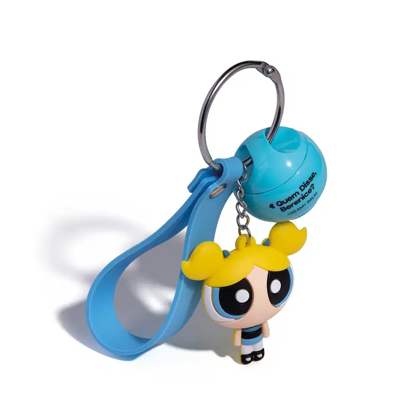 Chaveiro em formato da personagem Florzinha das Meninas Superpoderosas, com vestido azul e cabelo amarelo, preso a um produto da marca Quem Disse, Berenice?.