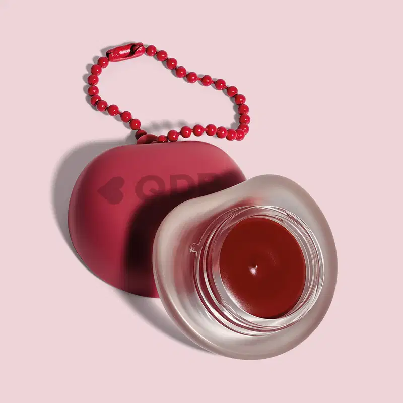 Recipiente vermelho com logotipo em forma de coração, O recipiente está sobre um fundo rosa. A imagem sugere um ambiente relacionado a produtos de beleza e cuidados pessoais.