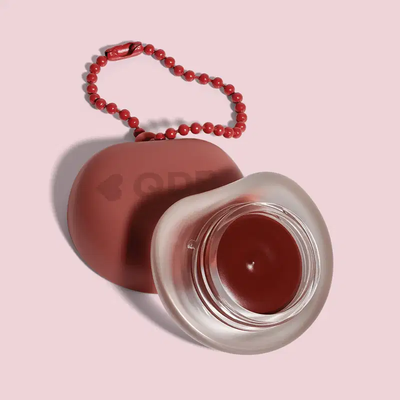 Recipiente marrom com logotipo em forma de coração, O recipiente está sobre um fundo rosa. A imagem sugere um ambiente relacionado a produtos de beleza e cuidados pessoais.