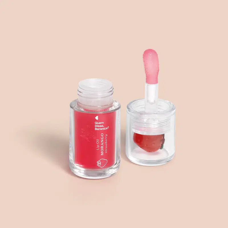 Imagem de um frasco transparente com tampa contendo o Lip Oil Cuide-se Bem Mrango da marca Quem Disse, Berenice. O produto é vermelho e tem aplicador em formato de esponja. Está em um fundo rosa claro com leve sombreado.
