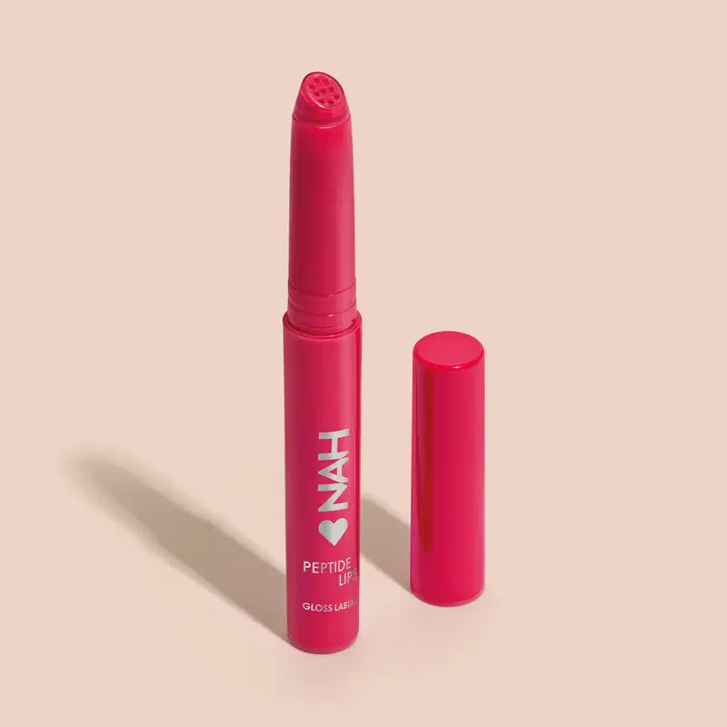 Produto de beleza em embalagem rosa, com rótulo "NAH Peptide Lip Gloss Labial". Apresenta formato de batom com tampa, em cor rosa vibrante.