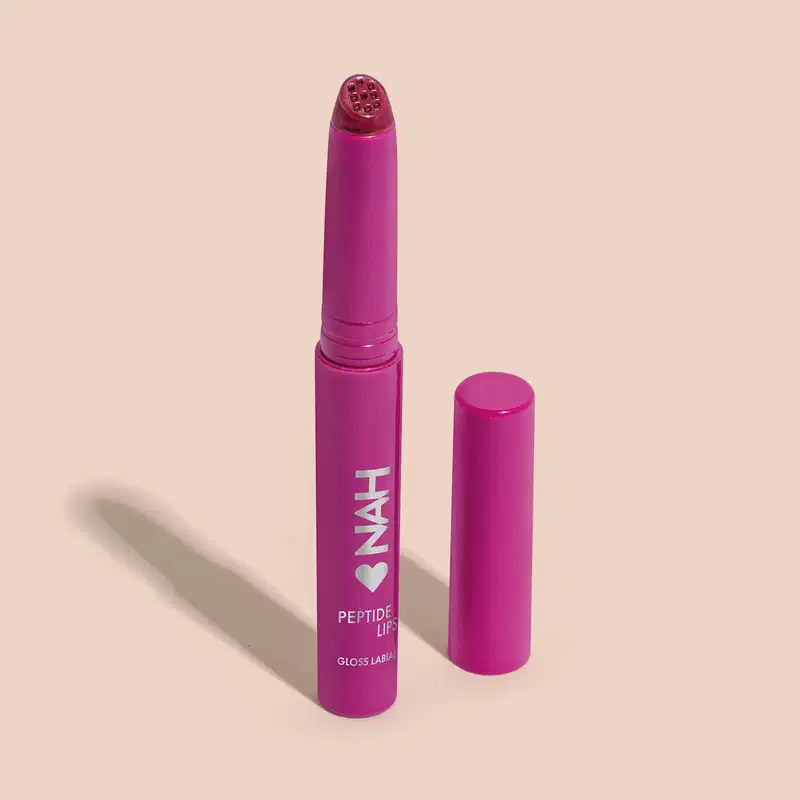 Produto de beleza em embalagem rosa vibrante, com rótulo indicando "Peptide Lips Gloss Labial". Formato de batom, com tampa destacável e corpo cilíndrico.