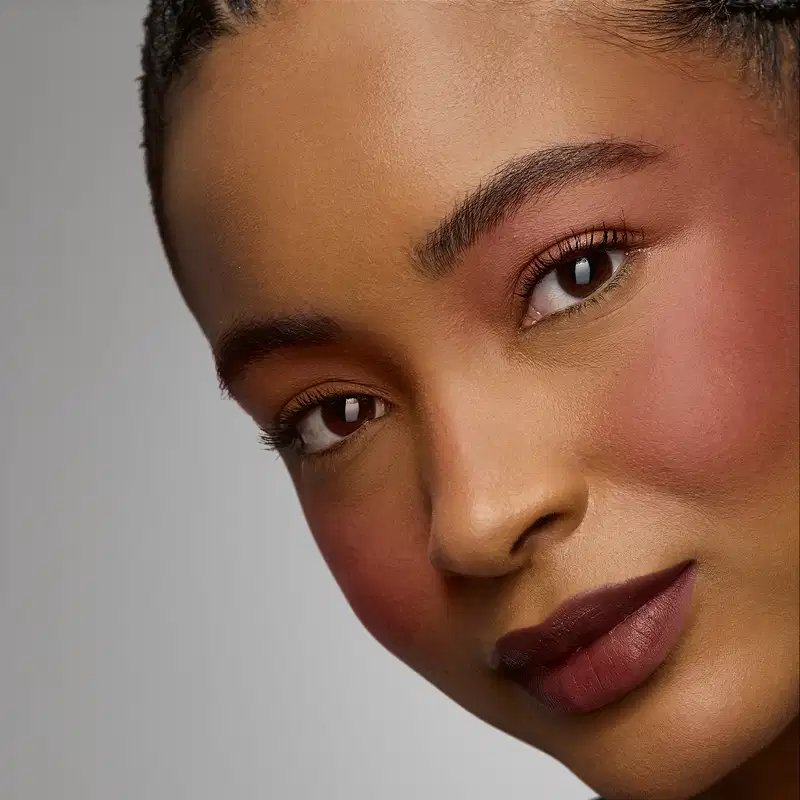 Rosto de uma pessoa com pele negra, olhos expressivos e lábios rosados. Fundo neutro e iluminação suave destacam os traços faciais. A imagem transmite uma sensação de beleza e elegância.