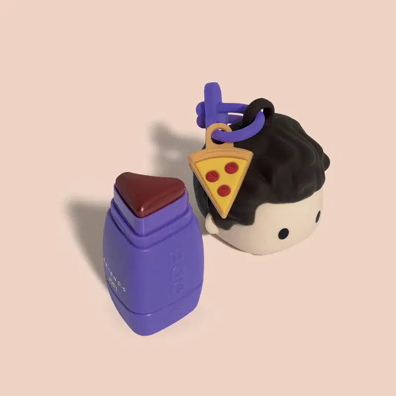 Um batom com tampa:um frasco roxo com tampa e um boneco, com uma fatia de pizza ao lado. 