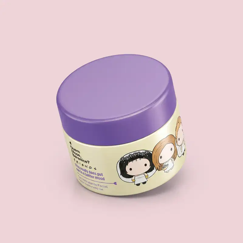 Recipiente de item de perfumaria em forma oval com tampa roxa. Embalagem de cor creme com ilustrações de personagens. Rótulo indica nome da marca "Friends" e menciona "Gel Hidratante Facial". Produto destinado a cuidados com a pele.
