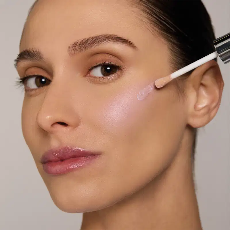Frasco de iluminador da marca Quem Disse, Berenice? em embalagem rosa clara com texto branco "NAH" e coração. Aplicador de espuma na ponta para aplicação suave do produto.