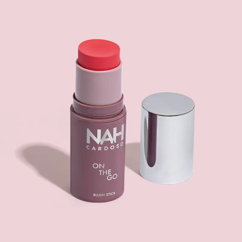 Produto de blush em bastão da marca NAH Cardoso, com embalagem roxa e tampa prateada. O rótulo indica "On the Go" e a cor do blush é rosa.