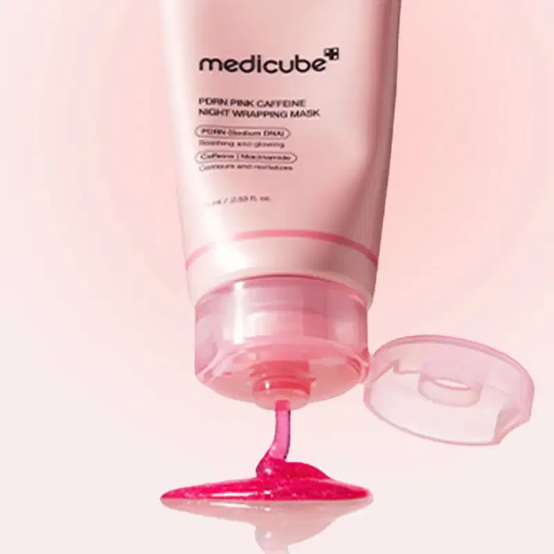 Um tubo rosa-claro da Medicube com máscara rosa vibrante escorrendo sobre superfície clara, em fundo rosa suave e minimalista, transmitindo ambiente de cuidado noturno com a pele.