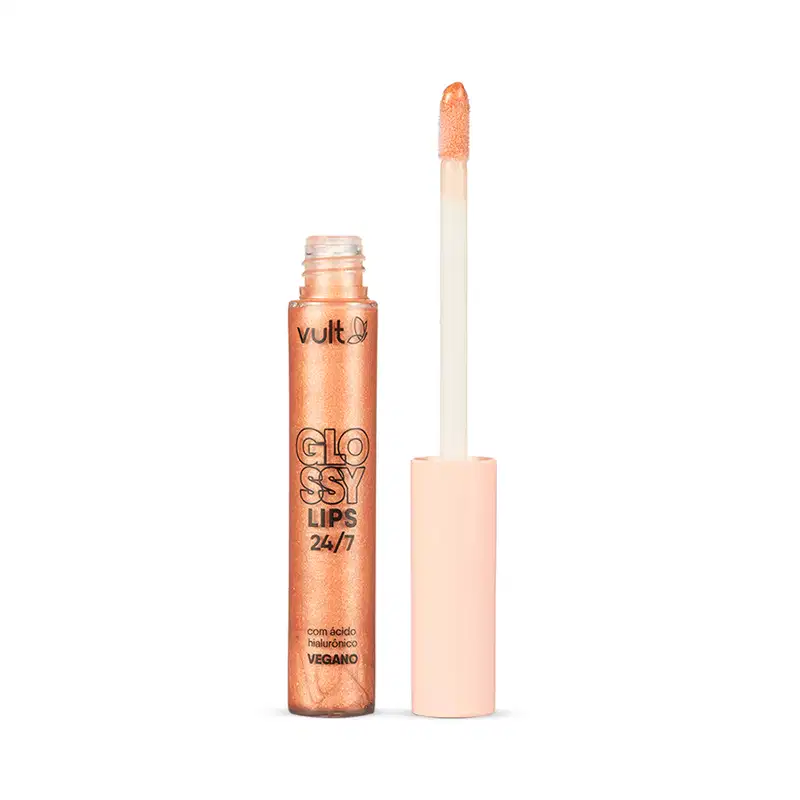Gloss labial em embalagem cilíndrica transparente contendo o gloss brilhante com tonalidade laranja claríssimo. Produto aberto com tampa salmão claro ao lado da embalagem. Rótulo em letras pretas no centro. Aplicador do tipo pincel firme.