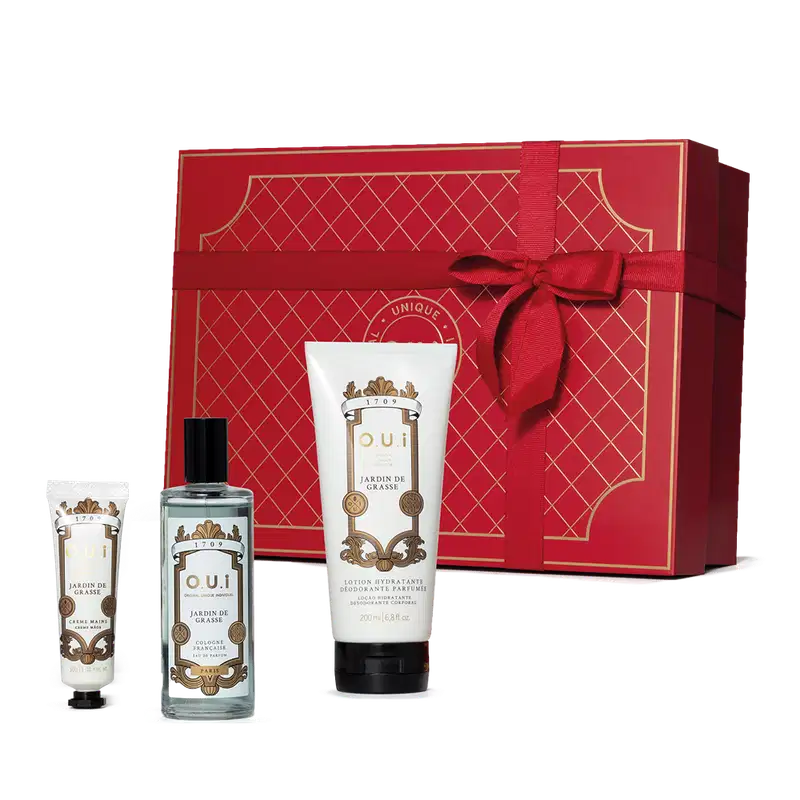 Conjunto. Frasco de colônia transparente com líquido azul claro e detalhes dourados no rótulo branco, um frasco de loção para mãos branco em forma de bisnaga e um tubo branco de loção hidratante. Todos com rótulo barroco com letras douradas e pretas.