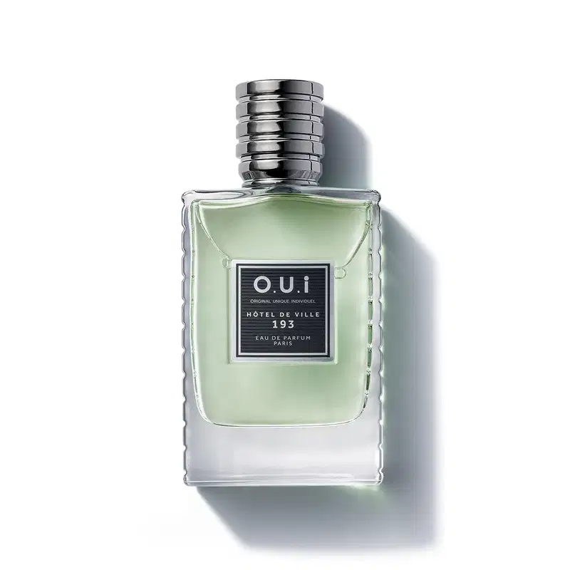 Frasco de item de perfumaria da marca O.U.i, com formato retangular, tampa prateada e rótulo preto com texto "HOTEL DE VILLE 193" em fundo verde claro.