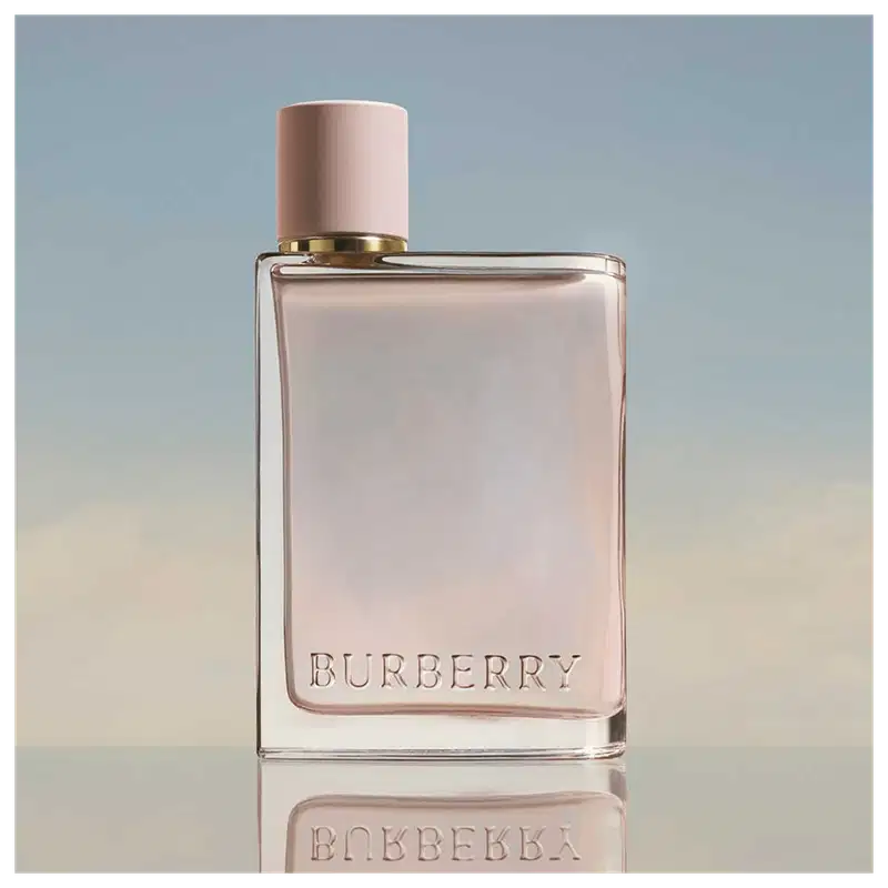 Frasco de perfume Burberry de cor rosa pálido com tampa dourada. O rótulo em destaque exibe o nome da marca "BURBERRY" em letras brancas.
