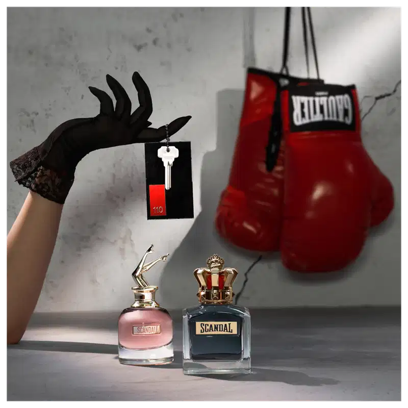 Ambiente de luxo e sofisticação com a marca Scandal da Jean Paul Gaultier. Caixa de presente, luvas pretas e luvas de boxe vermelhas criam um contraste entre elegância e força.
