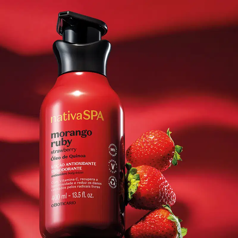 Frasco vermelho com bomba dosadora preta e letras douradas, brancas e pretas de loção antioxidante corporal Nativa SPA Morango Ruby sobre fundo vermelho, acompanhado de três morangos frescos ao lado.