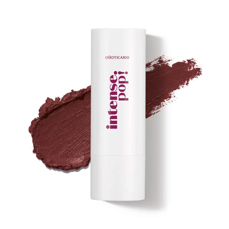 Batom de acabamento cremoso em embalagem branca com letras marrons, da marca Intense Pop! Atrás do produto, um rastro na cor bege amêndoa mostrando a textura e a intensidade do item.
