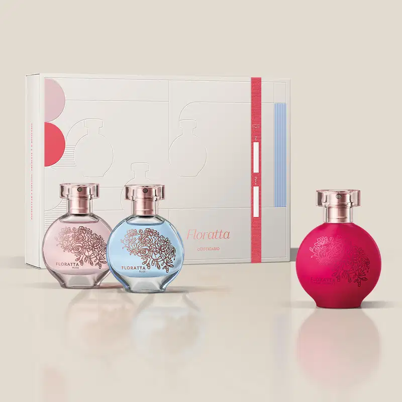 Três vidros redondos com florais em relevo, borrifador dourado e tampa cristal de desodorante colônia Floratta, sendo um rosa transparente da linha Rose, um azul transparente da linha Blue e um vermelho da linha Red, acompanhados de uma caixa de presente.