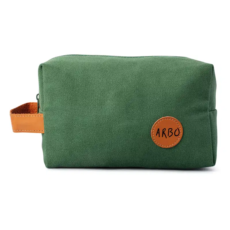 Nécessaire retangular de lona verde com alça de couro caramelo e logo Arbo em patch circular também em couro caramelo.