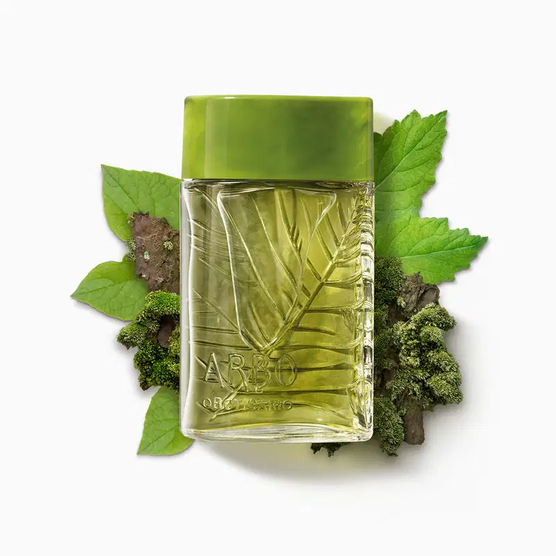 Vidro quadrado transparente com folhas em relevo, líquido verde e tampa verde musgo contendo 100ml de desodorante colônia Arbo Forest cercado por folhas verdes e musgo em superfície branca.