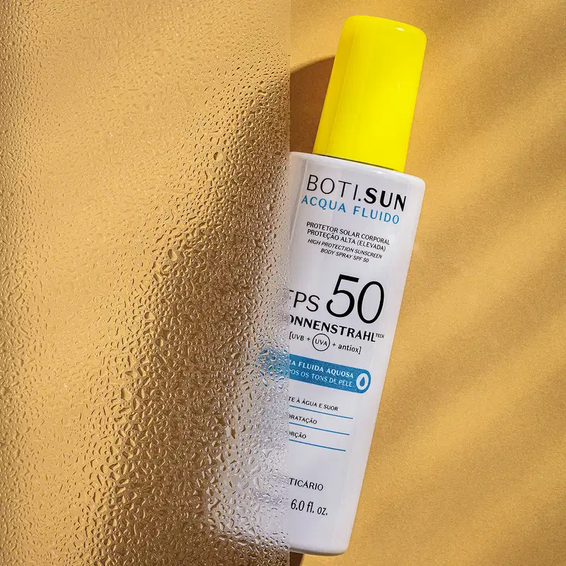 Frasco branco com tampa amarela, letras pretas e detalhe em azul, contendo 180ml de spray protetor solar corporal FPS 50 Acqua Fluído da marca Boti.Sun em fundo amarelo com sombras.