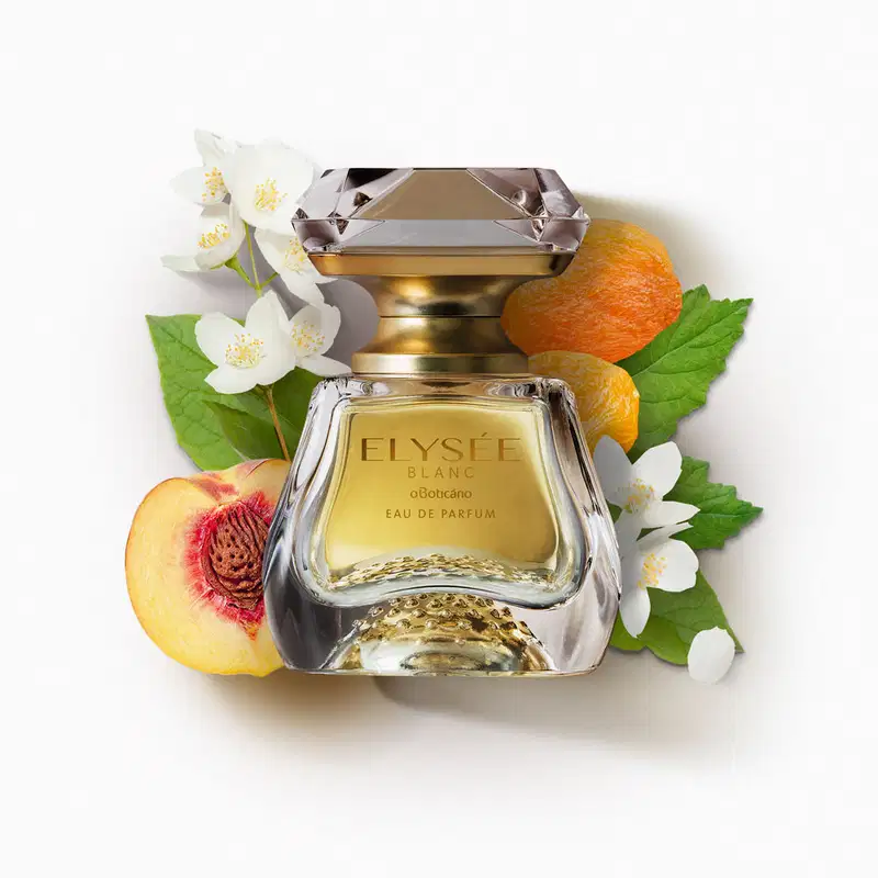 Vidro transparente com líquido bege, pulverizador dourado e tampa transparente simulando um cristal lapidado de Eau de Parfum Elysée Blanc cercado por flores brancas, pêssego cortado, laranjas e folhas verdes sobre superfície branca.