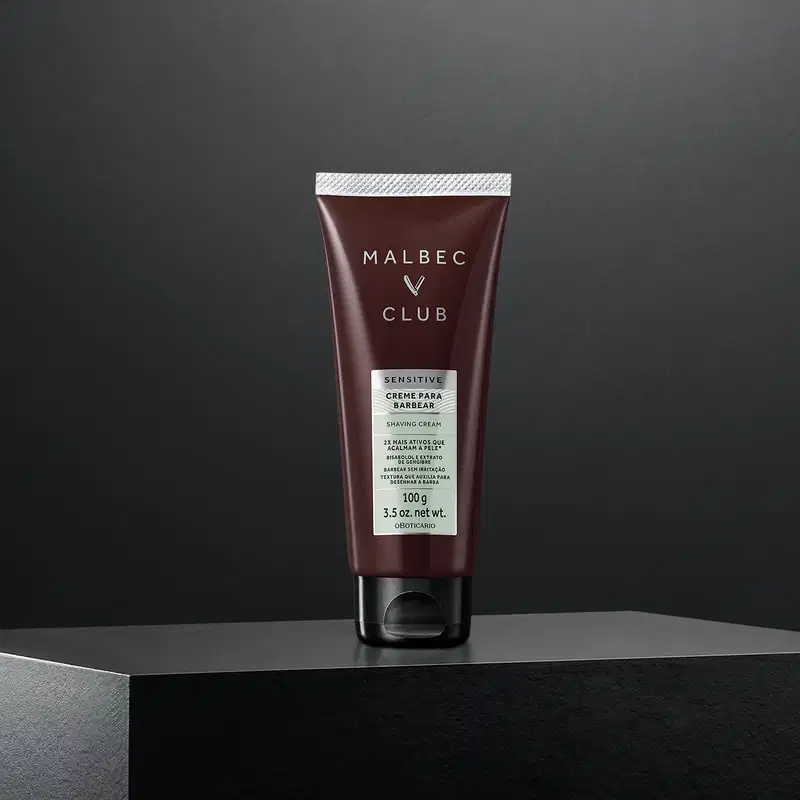 Tubo de creme para barbear da marca Malbec Club em fundo preto. O produto é descrito como "Sensitive" e possui embalagem em tom marrom escuro com detalhes em branco.