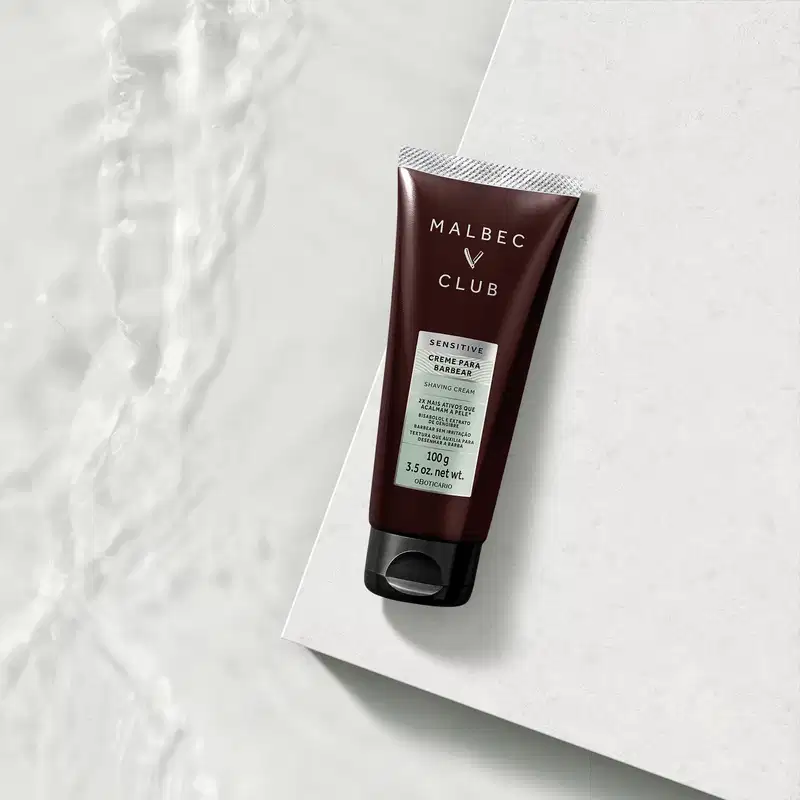 Tubo de creme para barbear da marca Malbec Club em fundo branco com textura de mármore. O cenário sugere um ambiente minimalista e elegante, adequado para o uso deste item de perfumaria.