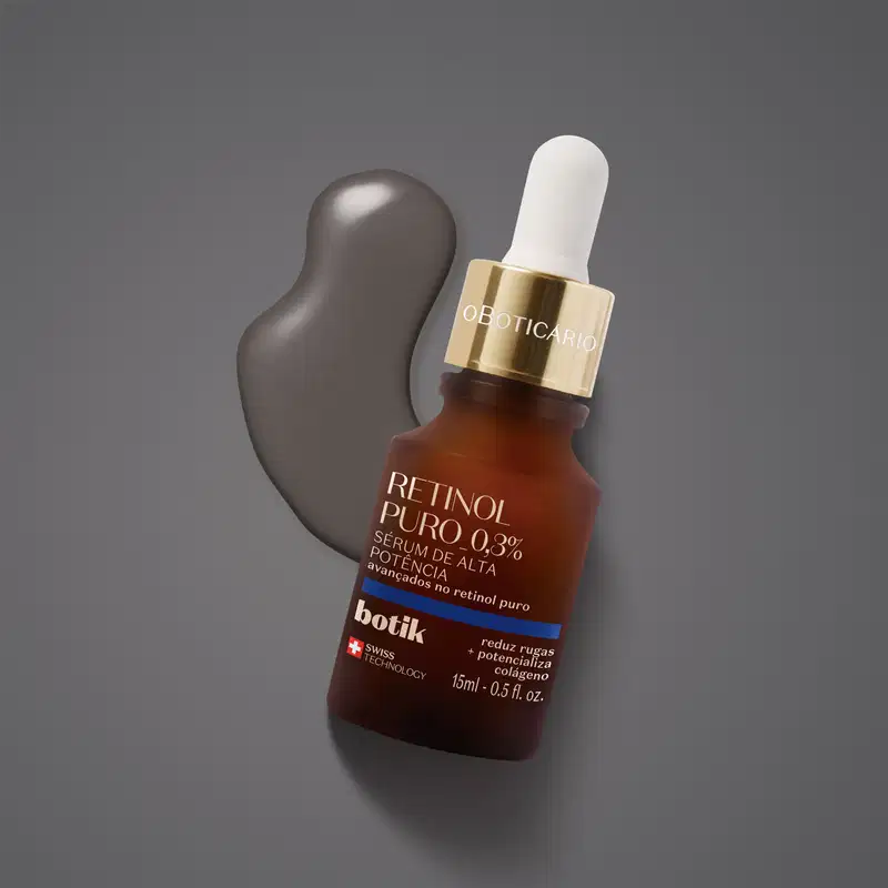 Vidro marrom com tampa dourada, conta-gotas branco, letras bege e detalhe azul contendo 15ml de sérum facial de alta potência Botik Retinol Puro sobre fundo cinza e uma pequena quantidade do produto espalhada atrás da embalagem.