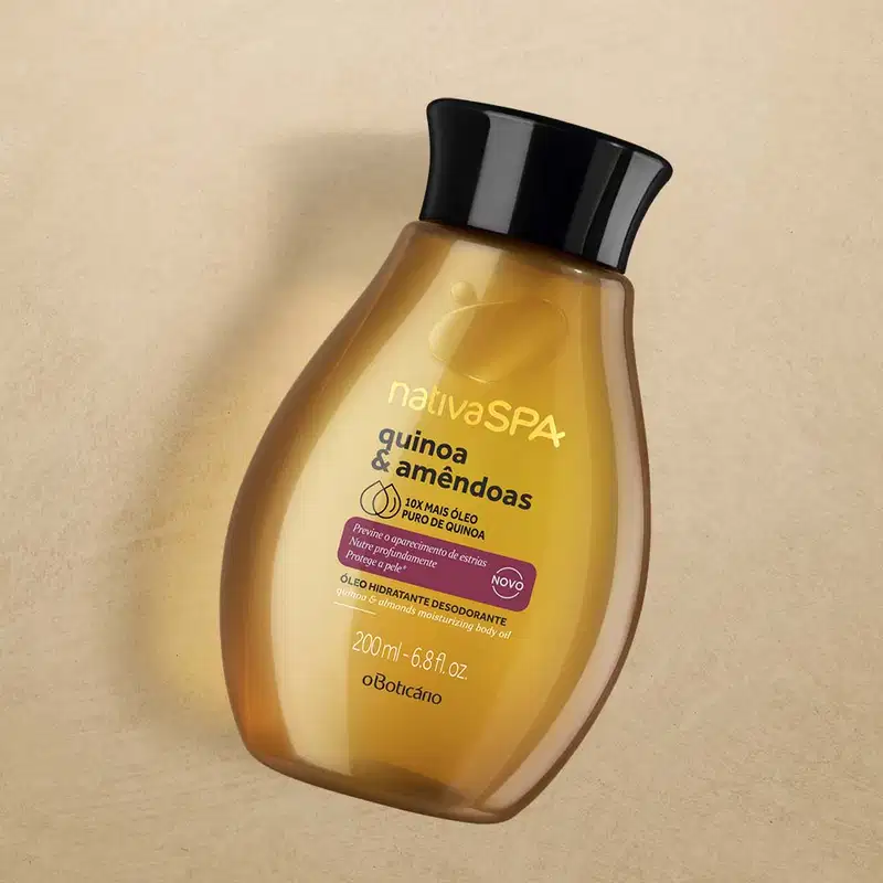 Frasco em formato oval marrom transparente, mostrando o líquido dentro, com tampa preta e letras douradas e pretas, contendo 200ml de óleo desodorante hidratante corporal da marca Nativa SPA Quinoa & Amêndoas em fumdo marrom.
