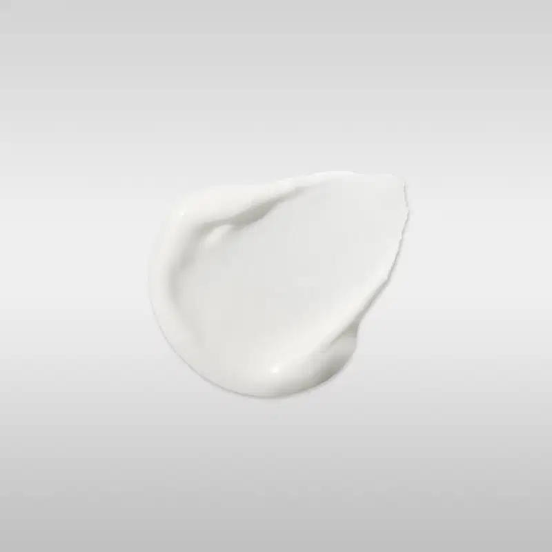 Textura de creme branco com acabamento brilhante e consistência densa, aplicado em superfície lisa com reflexo de luz destacando sua formulação cremosa.