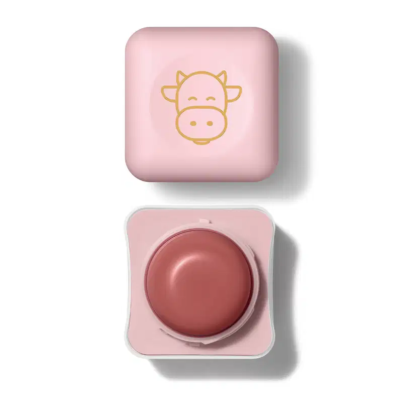 Pote compacto com cantos arredondados nas cores branca e rosa com roll-on rosa escuro e tampa rosa com ilustração de uma vaquinha contendo hidratante labial Intense & Cuide-se Bem Deleite.
