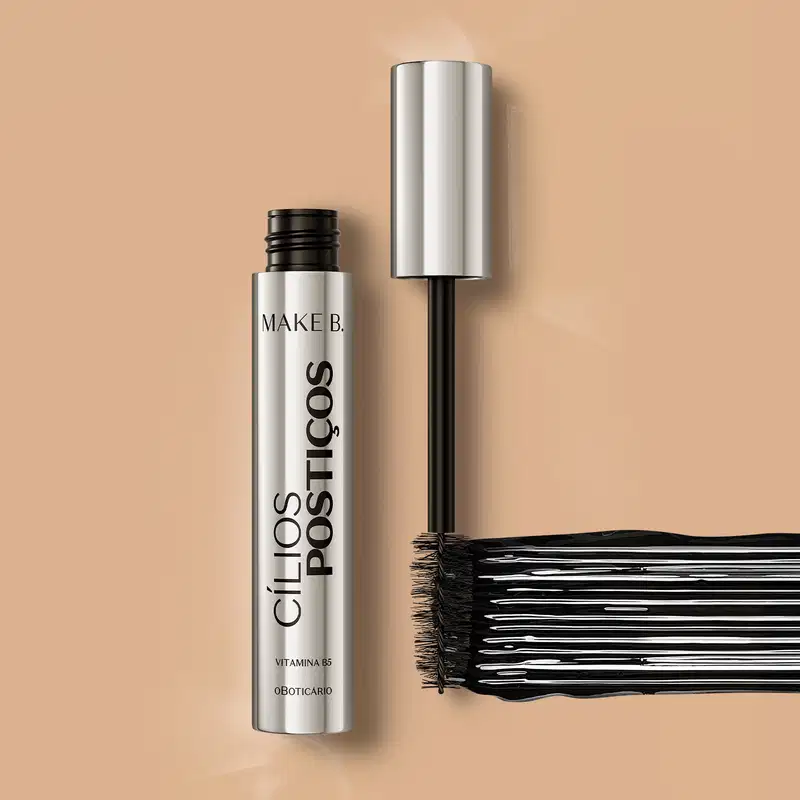 Tubo prateado com tampa na mesma cor, letras, haste e escova aplicadora pretas, contendo 10g de máscara de cílios Make B. Efeito Cílios Postiços. Há um rastro do produto mostrando a cor e a intensidade.