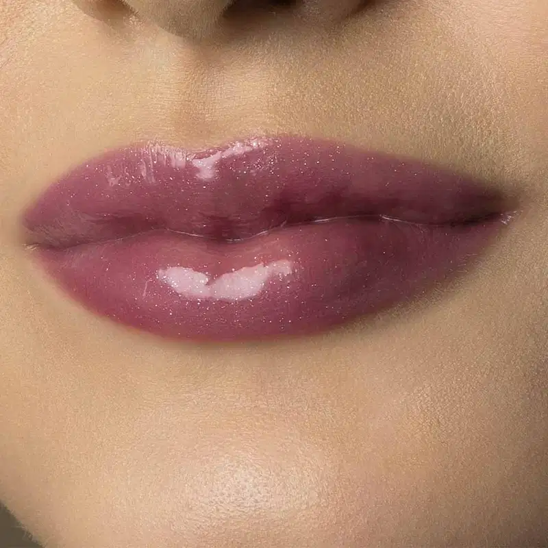 Close-up de um rosto feminino de pele branca evidenciando os lábios brilhantes e rosados que usam o gloss labial Rose Lover da marca Make B. 