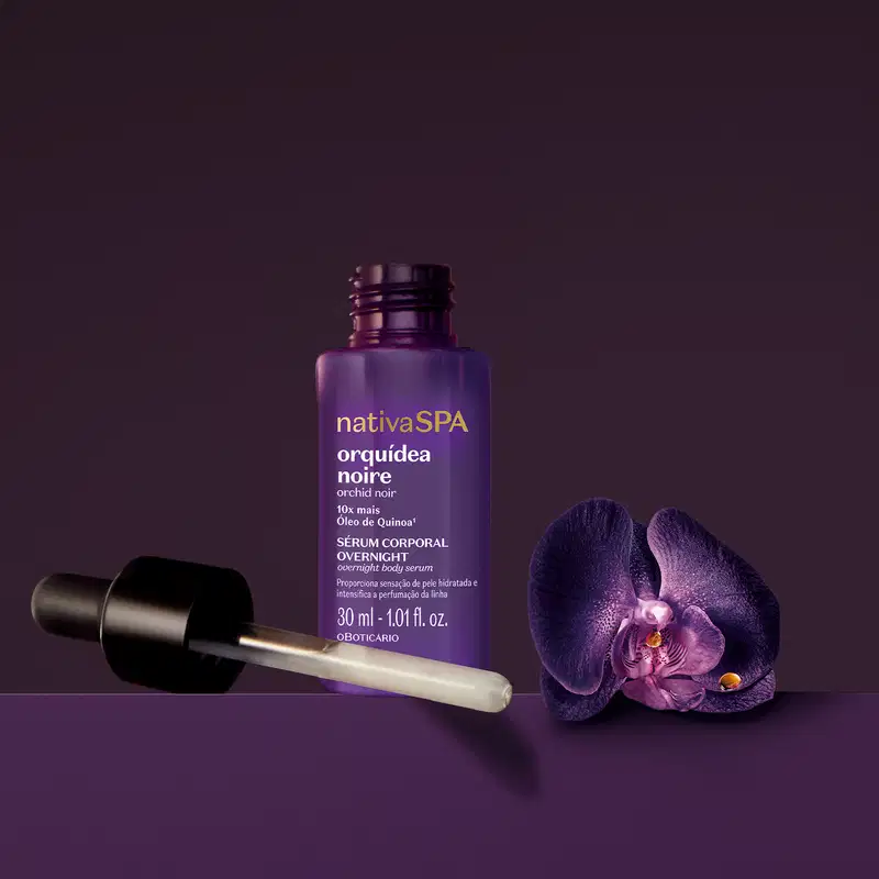 Frasco roxo com conta-gotas preto e letras douradas e brancas de sérum corporal overnight da marca Nativa SPA Orquídea Noire em fundo escuro com orquídea roxa ao redor.