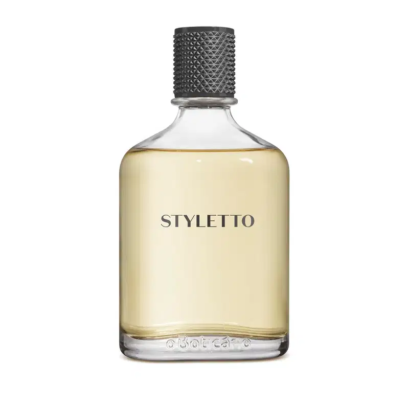 Frasco de fragrância Styletto com tampa preta texturizada e rótulo em letras pretas sobre fundo amarelo claro. O frasco é de vidro transparente, permitindo visualizar o conteúdo líquido.